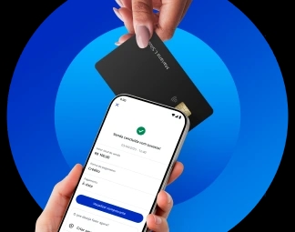 Mão segurando um celular que exibe o comprovante da venda enquanto outra mão segura um cartão de crédito próximo ao celular.